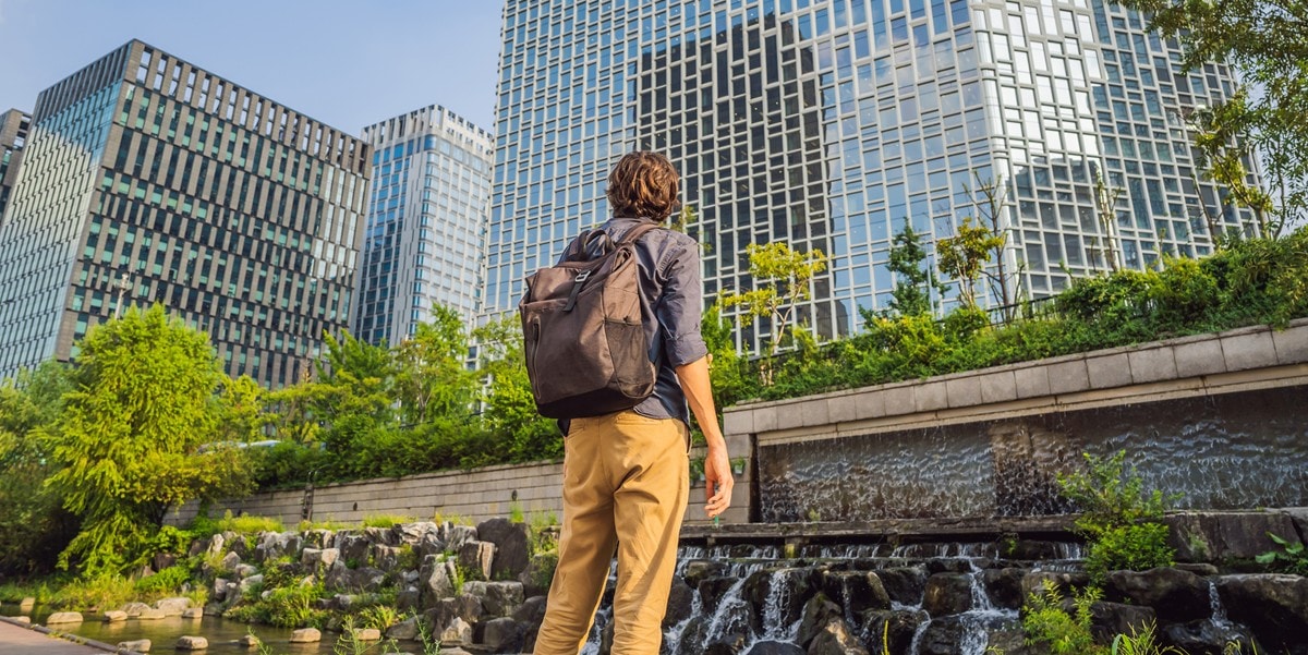 man standing outside with backpack, looking up at a building