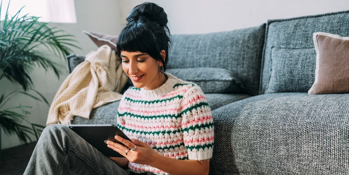 woman working at home, sitting in front of a couch, using a tablet