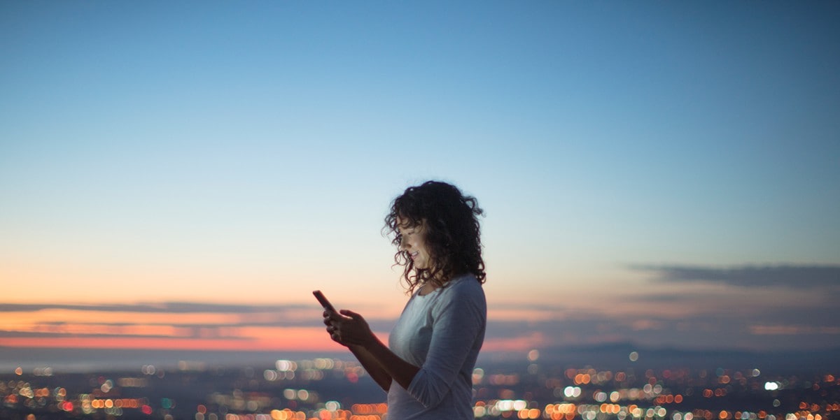 woman standing outside at dusk using cellphone