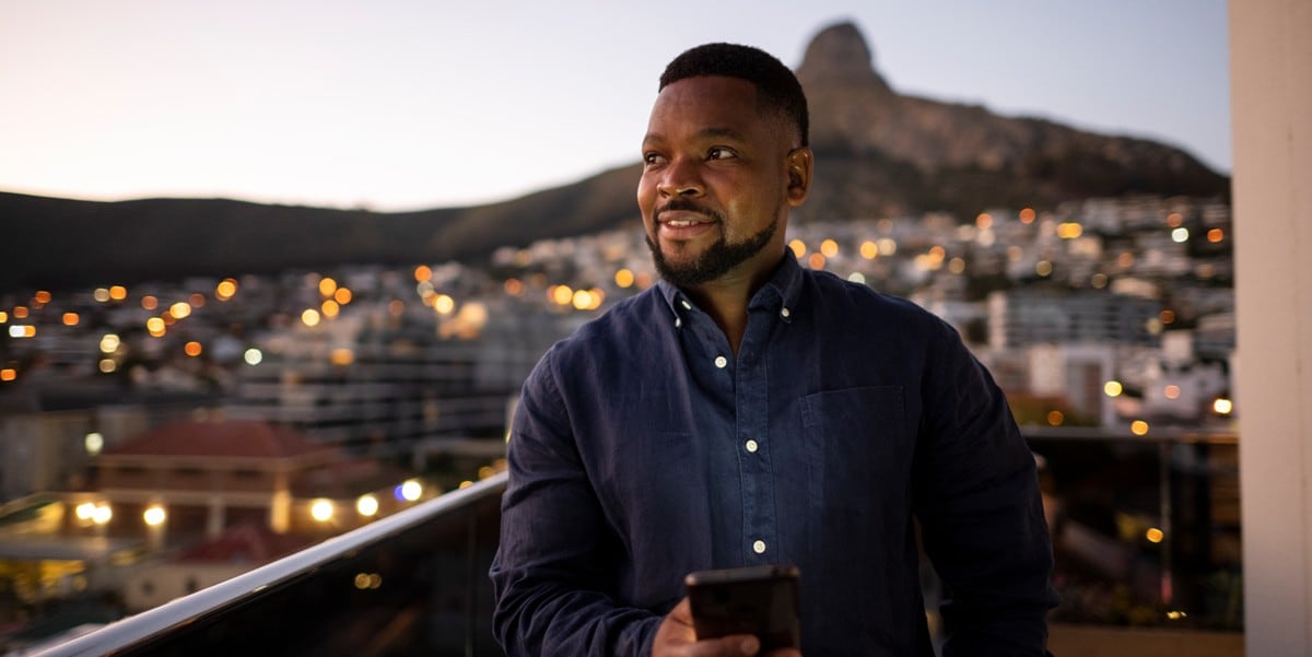 man standing outside holding cell phone, city behind him