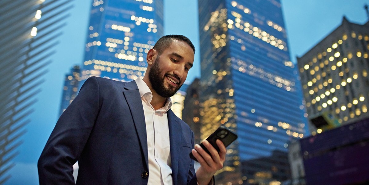 man looking down at cell phone, skyscrapers behind him