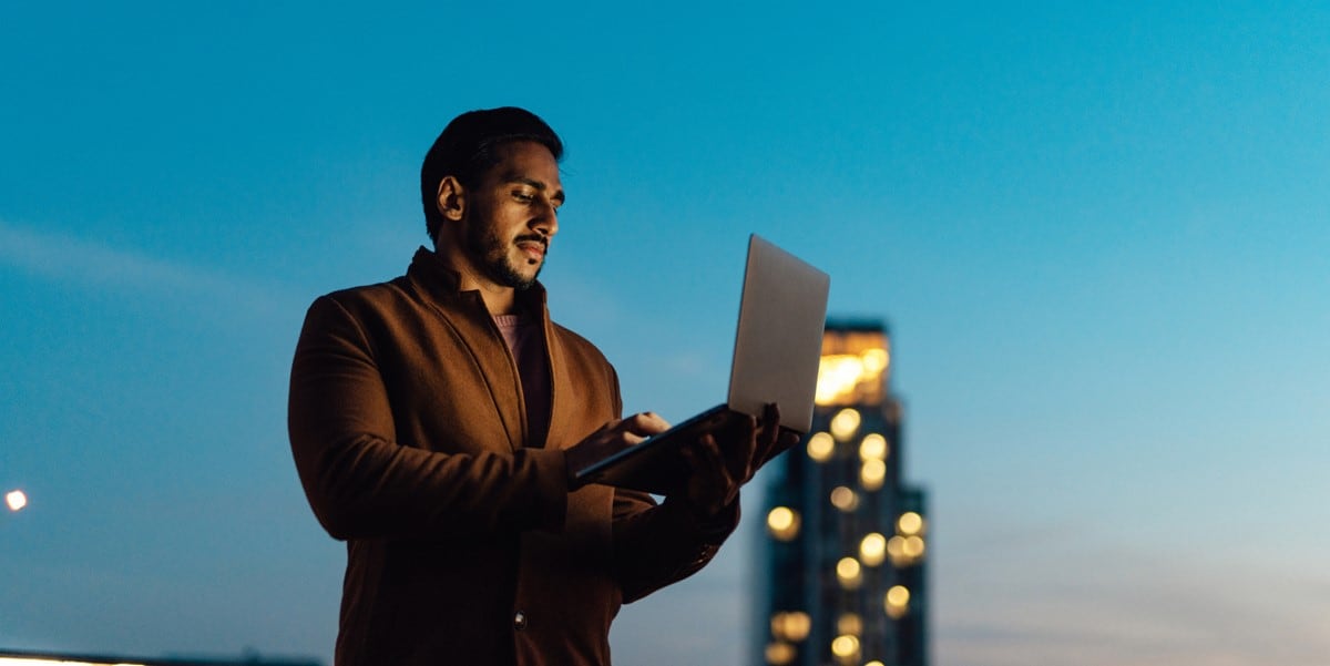 man standing outside holding laptop, office building behind him