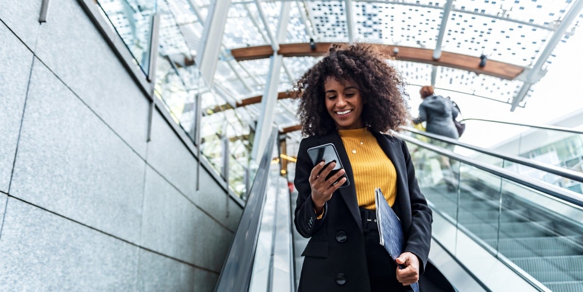 woman traveler going down an escalator, using cell phone