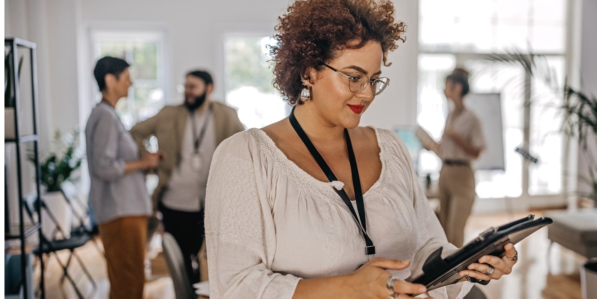 woman in office, looking at tablet, colleagues in the background
