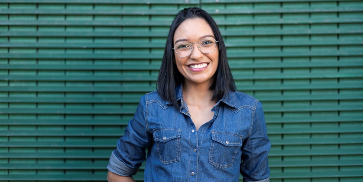 woman with glasses smiling in front of green wall