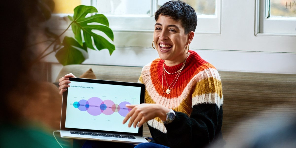 woman in office pointing at presentation, holding laptop