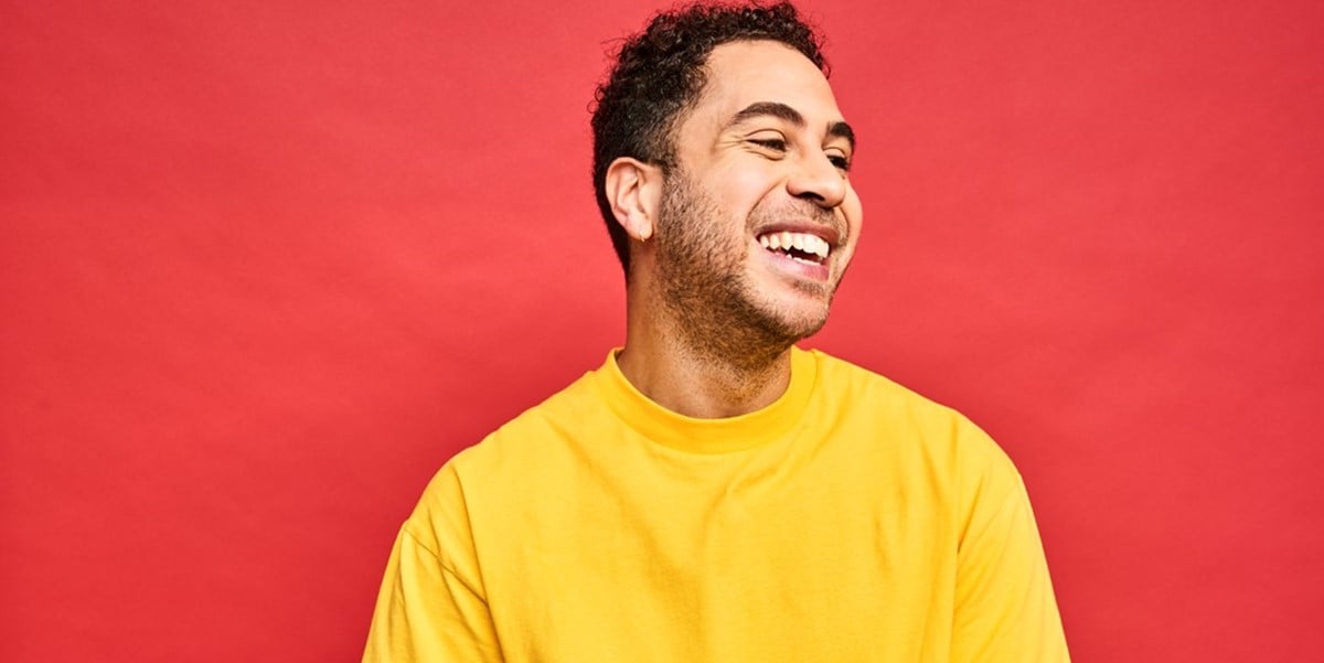 man in yellow sweater smiling, red background