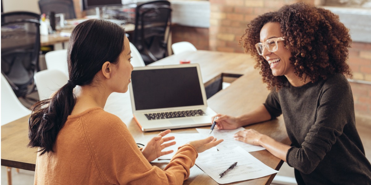 two women talking and working together next to a computer