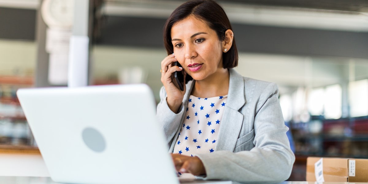 woman working at a desk using laptop and cellphone