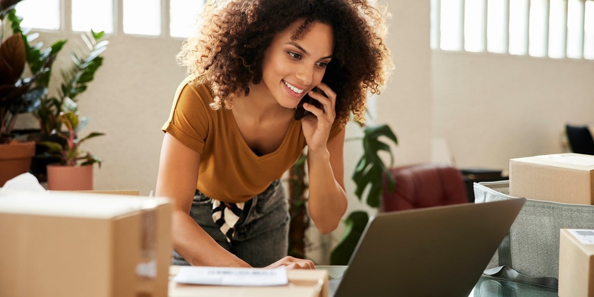 woman on the phone looking at laptop on desk